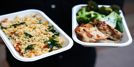 A person in a black shirt holding a rice dish and meat dish in both hands
