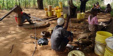 Villagers sitting and standing around water barrels