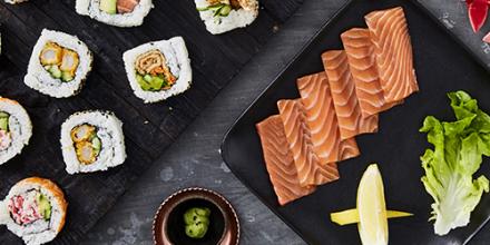 A tray of sushi rolls and sashimi, with bowls of pickled ginger and soy sauce