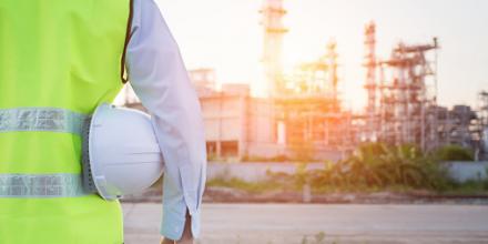 An energy worker stands with his back to the camera with electrical lines in the background