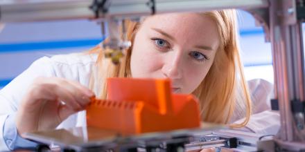 A female student inspects her bright orange additive 3D printed object