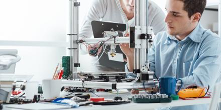 Two men working together at a workstation full of electronic research equipment