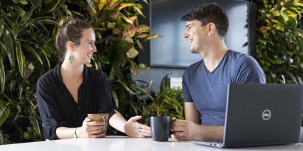 Two students sit at a bench discussing their research over coffee