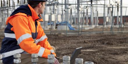 A man in a high-visibility jacket squatting down at a power station