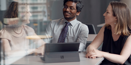 Three colleagues, a man and two women, sitting around a table with a laptop.