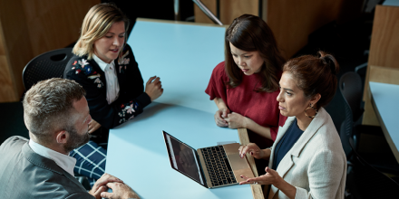 Four colleagues at desk working around a laptop