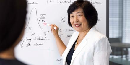 Distinguished Professor Jie Lu wearing a white jacket. She is discussing machine learning theory with a colleague while standing in front of a whiteboard with her pen poised