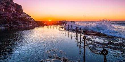 A pink sky at sunrise with ocean pool in the foreground.