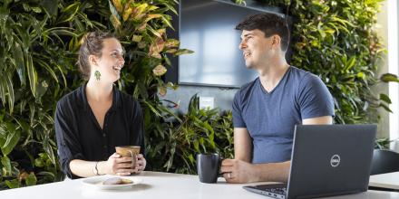 A woman and a man sit at a bench, talking and drinking tea.