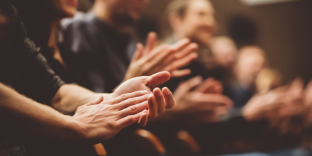 A close-up photo of people sitting in an audience applauding something.