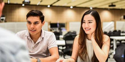 Two students sitting together socialising with other colleagues