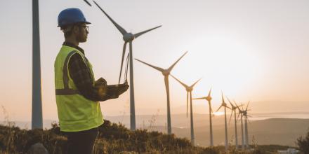 Solar engineer on laptop overlooking wind turbines