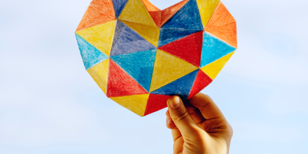 Hand holding up mutli-coloured paper heart.