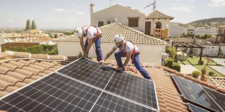 Two workmen install solar panels on a suburban rooftop