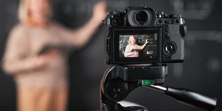 Teacher pointing at blackboard and recording lesson on professional camera