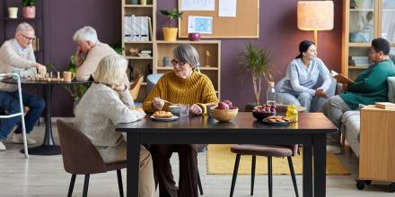  Full length view at common room in retirement home with diverse group of seniors enjoying leisure activities