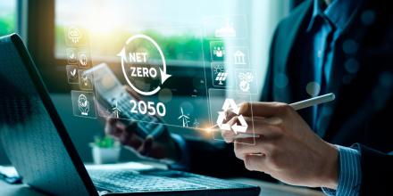 Man at laptop with pen and calculator in hand with Net zero by 2050 and a number of icons displaying on a screen