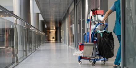 Cleaner pulling cleaning trolley down hallway