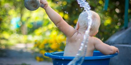 Photo of the back of a toddler bathing in a plastic tub and tossing water