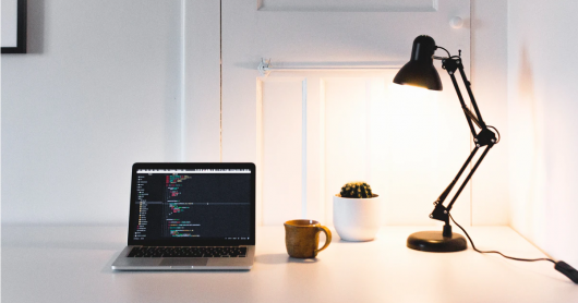 open laptop and mug on desk with lamp turned on