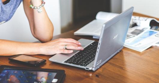 A young woman sits at a table with a laptop, mobile and tablet