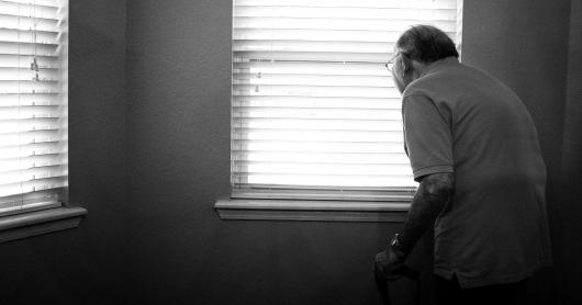 An elderly man in a white room near two windows.