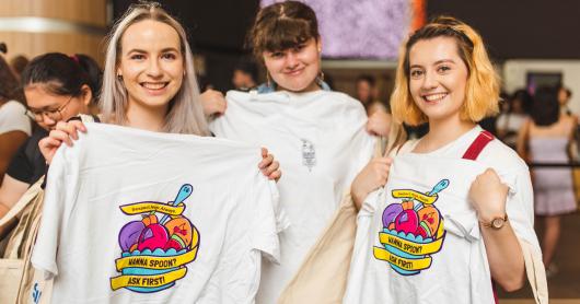 Three students hold up t-shirts with the Respect.Now.Always campaign branding.