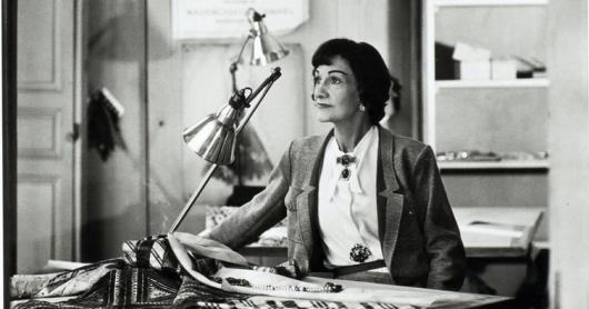 Coco Chanel sitting at a desk.