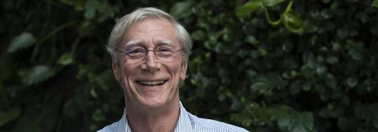 a man smiling at the camera green foilage behind him