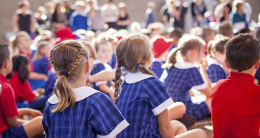 A group of school children sitting on the ground looking forward