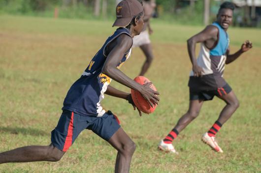 Young Indigenous men play AFL on a grassy field