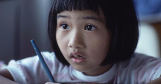 A student looks attentively towards the front of the classroom with pencil poised to write.