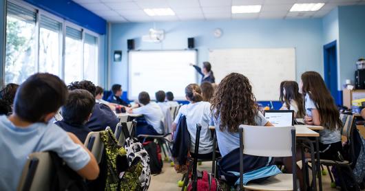 view from the back of a class of a high school classroom: students face a teacher 