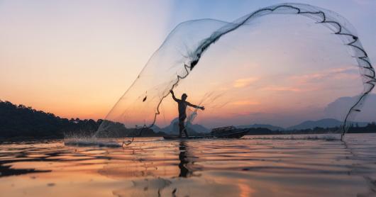 Fishermen throwing fishing net during twilight on wooden boat at the lake.