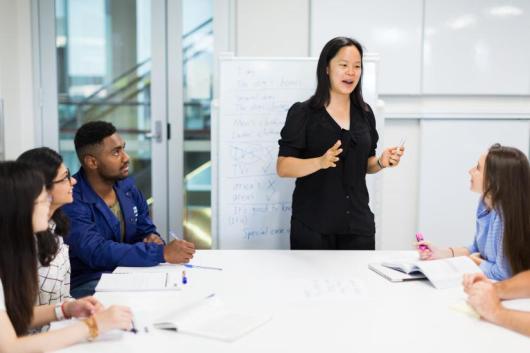 Image of five people in a classroom. One person is teaching the others.