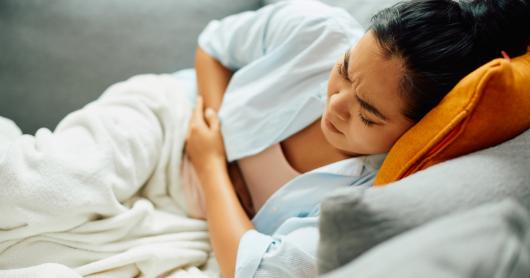 A woman winces in pain, her hands clutched at her belly