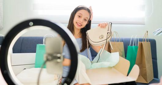  a smiling child holds a handbag up to a mobile phone camera