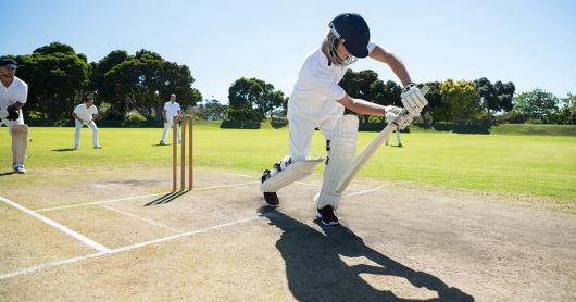 Cricket player in whites demonstrating a cricket stance blocking at a park