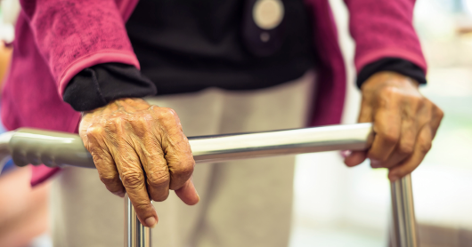 An older person stands with the assistance of a walking frame.