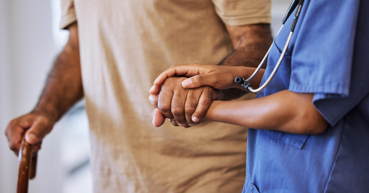 A caregiver or nurse supports a senior man or patient walking