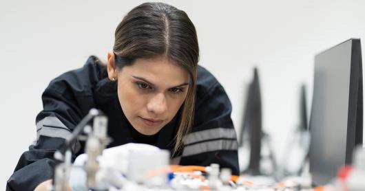 A woman working closely on electronic machinery