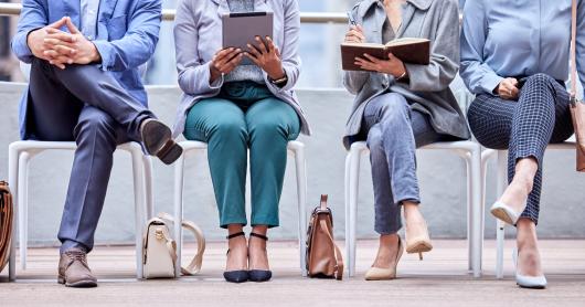 A group of unidentified workers seated in a row holding iPads, notebooks and a pen.