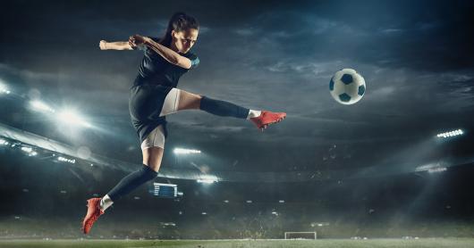 Football player leaping to kick ball in stadium