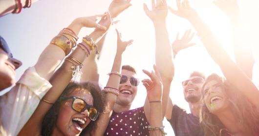 A group of people gathered at a festival with their hands in the air and looking excitedly in the distance.