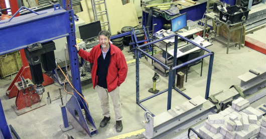 A man stands in a workshop, looking up at the camera