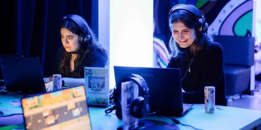 Two women wearing earphones and looking at computer monitors