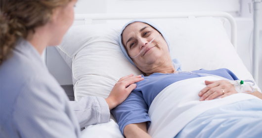 Senior women with head scarf smiles at carer from hospital bed