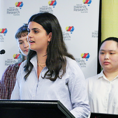 3 females presenting, one stands at a lectern.