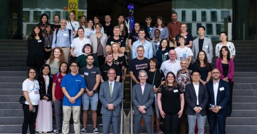 A large group of smiling people pose for a photo on the steps of UTS Building 2.
