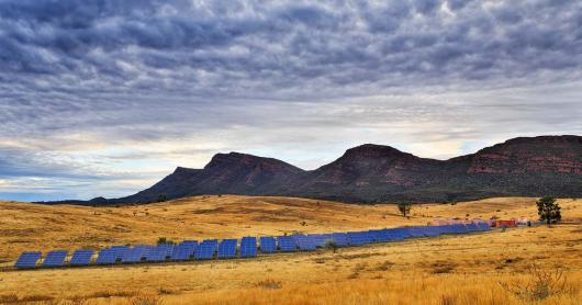 solar panels in a grassy landscape, hills and clouds in background